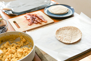 Tortilla sits on wax paper next to bacon and eggs, ready for meal prep