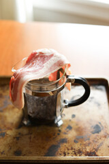 Raw slices of bacon over French press coffee maker