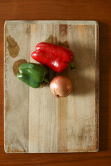 Fresh red and green pepper next to onion on cutting board