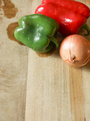 Closeup of Fresh red and green pepper next to onion on cutting board