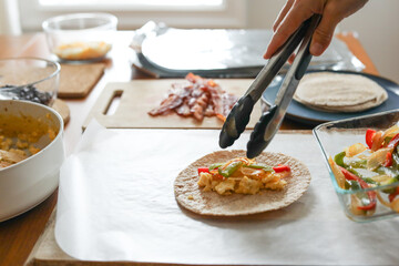Woman places peppers on tortilla for meal prep breakfast burritos