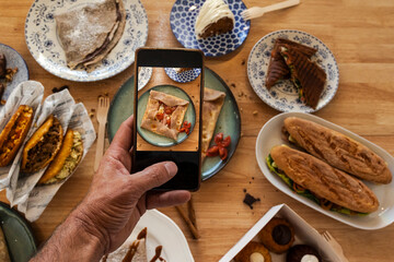 Hand holding smartphone photographing food on table