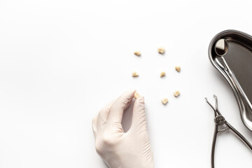 Dentist hand in white medical glove is holding teeth crown for dental implantation on white background. Professional Dentist desktop, top view