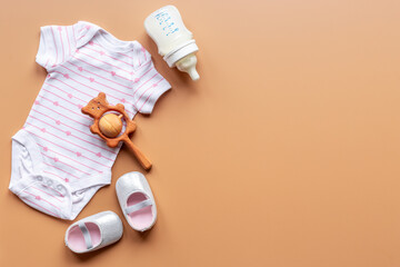 Baby bodysuit with wooden teethers and bottle of milk on pastel beige background, top view
