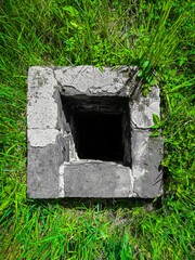 Overhead view of a square concrete manhole or well opening surrounded by bright green grass
