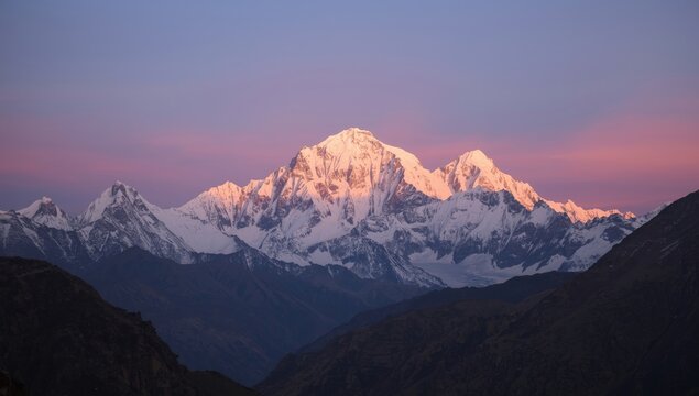 Majestic snow-capped mountain range illuminated by the soft golden light of sunrise or sunset, creating a stunning visual display against a backdrop of pink and purple hues in the vast expanse..