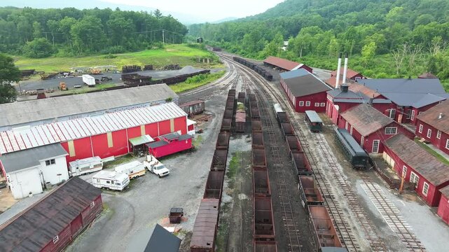 This location features a vast, abandoned train yard with rusty train cars and historic industrial buildings. Surrounded by lush green mountains, it showcases a piece of transportation history.