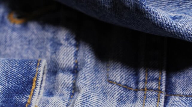 A blue denim jacket reveals twill texture, orange stitching and a metal rivet as the camera pans slowly left to right