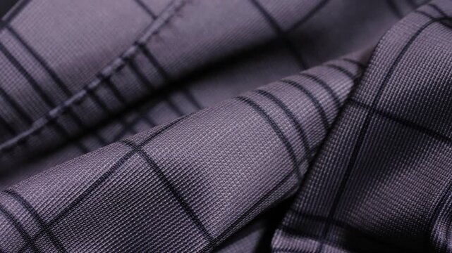 Grey striped polyester trouser fabric with folds and fine grid pattern, slow macro pan