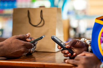 Mobile money cashless digital payment, African businesswoman assists a customer with mobile money transaction in her supermarket © Roger