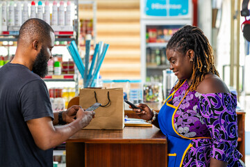 Mobile money cashless digital payment, African businesswoman assists a customer with mobile money transaction in her supermarket
