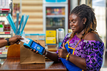 Contactless payment, African businesswoman processing cashless transactions for a customer in her supermarket via point of sale POS device
