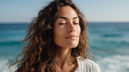 A woman with long brown hair is sitting on the beach, looking out at the ocean