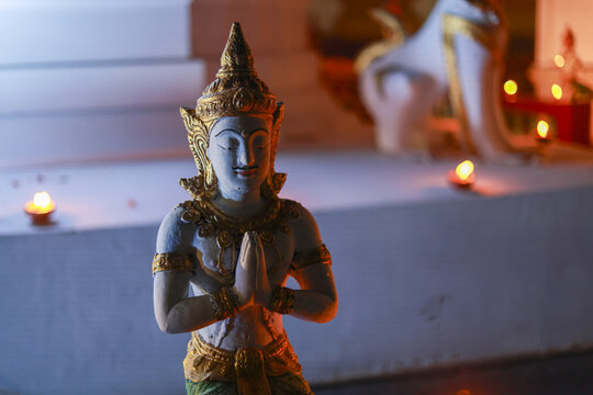 Serene Thai Buddhist Thepanom statue in greeting pose with hands clasped in prayer. peaceful sculpture sits in tranquil temple illuminated by warm, soft candlelight