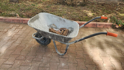 A weathered wheelbarrow used for construction or gardening, holding a few bricks, resting on a...