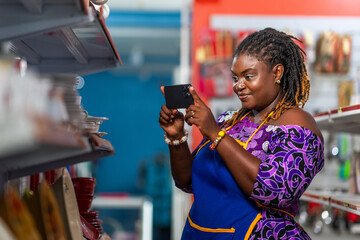 African businesswoman captures product photos with her smartphone in her supermarket for online marketing on social media © Roger