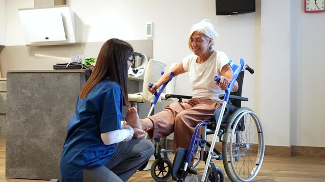 Professional female nurse providing home care and physical therapy to a senior woman in a wheelchair, massaging her foot for rehabilitation after an injury with a friendly and supportive attitude