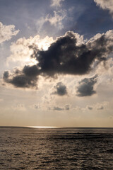 Naklejka premium sunrays shining through dark clouds over a calm ocean