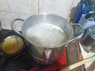 Boiling soup in a stainless steel pot on a stove — homemade broth cooking process with steam and foam.