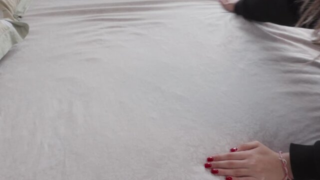 Girl in black sweater stroking and flattening white striped fabric on bed, making bed or bedroom tidying activity 