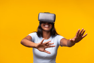 Young woman exploring virtual reality using headset and interacting with digital world on yellow background