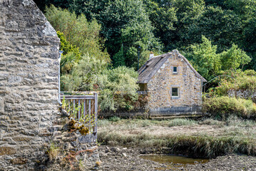 Old stone cottage by the Goyen river with stone wall and lush green forest surroundings, in the village of Pont-Croix in the Finistere department, in Brittany, France