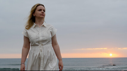Fototapeta premium Enjoying a tranquil and serene beach walk at sunset while wearing a lovely white dress