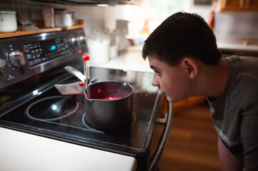 Teen carefully watching red candy mixture cook on home kitchen stove