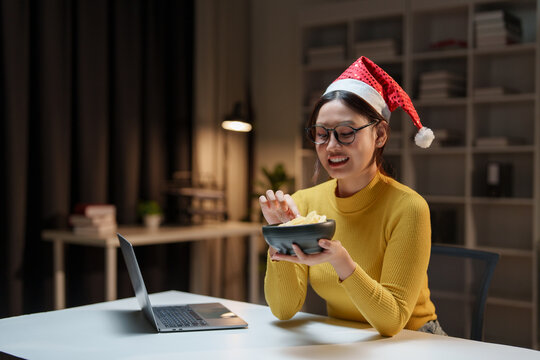 Woman wearing santa hat eating chips while having video call - Powered by Adobe