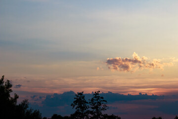 Captivating sunset sky ablaze with orange, pink, and blue. Golden clouds drift above a tranquil twilight landscape, framed by dark tree silhouettes