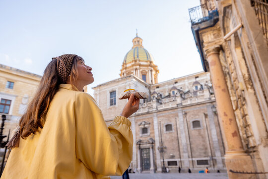 Smiling woman holding a traditional Sicilian cannolo in the historic center of Palermo, Italy. Joyful travel moment and authentic local experience
