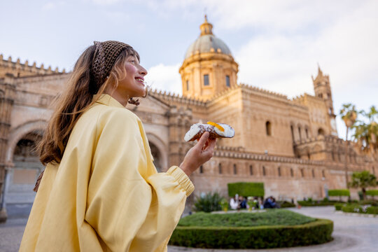 Back view of woman holding a traditional Sicilian cannolo while admiring Palermo Cathedral. Travel, culture, and slow living in the heart of Sicily