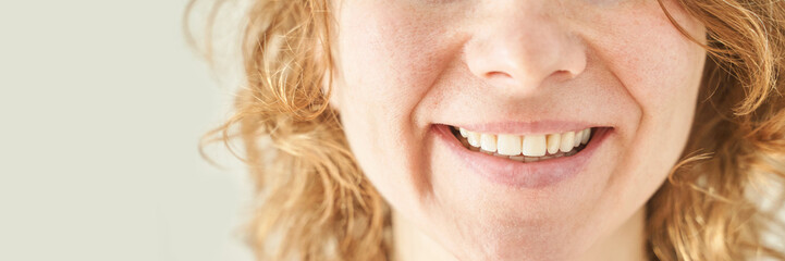 Close-up of smiling caucasian female with curly hair and freckles displaying natural teeth and joy.