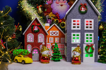 In the Christmas village there are three colorful houses surrounded by Christmas trees and snowmen