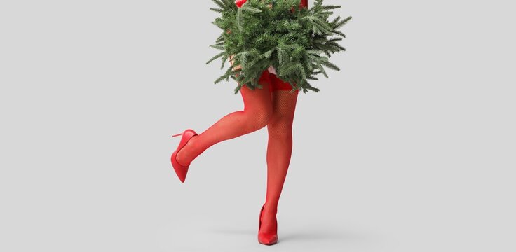 Legs of young woman in red stockings and with fir tree branches on light background