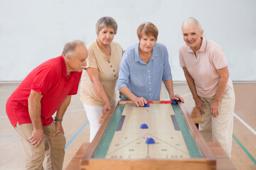 senior group Playing the board game of shuffleboard.  Kidult gaming in the gym. Active retirement...