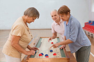 senior group Playing the board game of shuffleboard.  Kidult gaming in the gym. Active retirement...