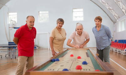 senior group Playing the board game of shuffleboard.  Kidult gaming in the gym. Active retirement...