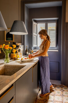 Woman preparing food in a cozy Sicilian kitchen with gray walls, vintage tiles, and warm morning light. Slow living and Mediterranean home atmosphere