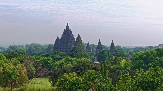 Aerial view of Prambanan Temple emerges from the green canopy, ancient spires piercing the skyline, Yogyakarta, Daerah Istimewa Yogyakarta, Indonesia.