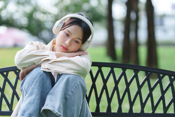 Young asian woman feeling sad listening music park bench