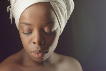 Portrait of Black Beauty. Headshot of young beautiful African woman in white turban with bare shoulders looking down on dark background