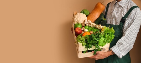 Male farmer with box of vegetables and fruits on beige background with space for text, closeup