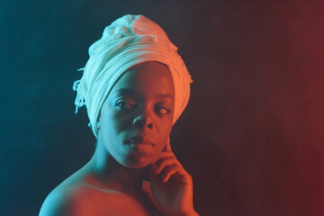 Waist-up portrait of young pretty African woman in white headwrap with bare shoulders looking aside...