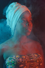 Waist-up portrait of attractive African woman in swimsuit and headwrap standing standing on dark...