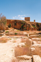 Distant view of a rocky hilltop in Fes, Morocco, featuring an ancient ruined wall and dry desert landscape under clear blue sky.