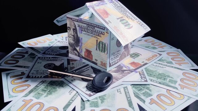 House made of American currency banknotes and key on money background. Mortgage and savings concept. Selective focus.