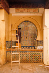 Abandoned traditional Moroccan fountain in the old town of Fes, with ladder and unused objects surrounding the worn structure.