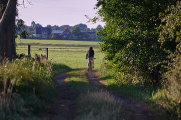 Rear view cyclist biking rural pathway green countryside farmhouse background summer recreation Germany horizontal landscape