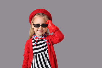 Stylish little girl in red beret with sunglasses on grey background